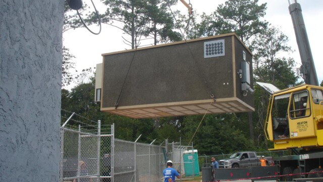 A crane lifting an equipment shelter into place for its associated radio tower