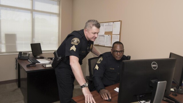 officer at desk looking at computer with another officer standing beside him