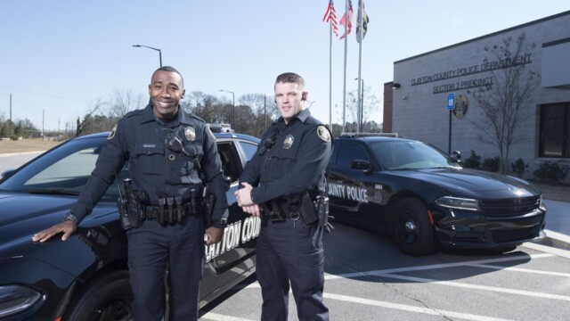 2 police officers in front of police cars by the building
