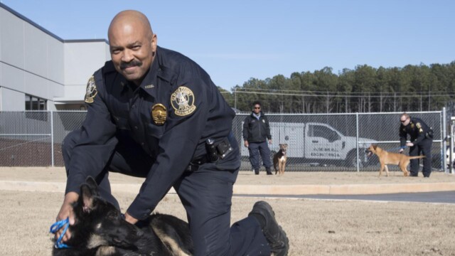 Leashed dogs with their police officers outside of an Animal Center, looking at camear