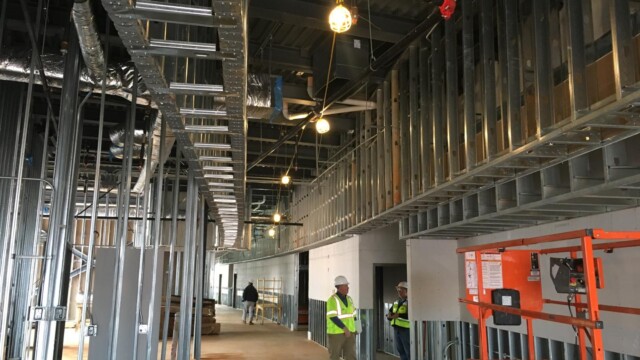 inside building showing metal beams and several workers