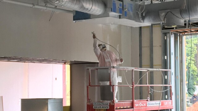 Painter on mobile lift platform, painting overhead ductwork