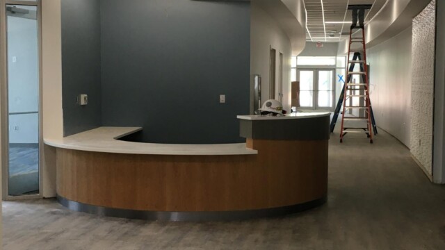 concierge desk next to hall with man on top of ladder half inside ceiling