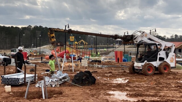 Construction workers using a skid steer machine to bore and sink helical pile metal pipes into the ground for building structural foundation