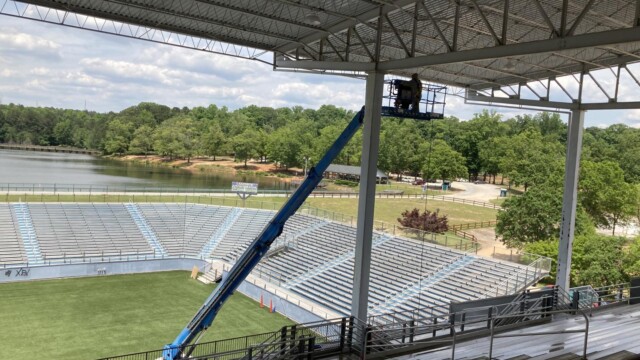 Person on a boom lift platform underneath the roof over a stadium seating area at VIP Complex