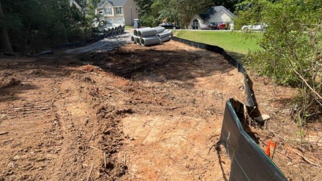 freshly dug up land with concrete tubes and a home in the background