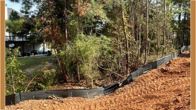 freshly dug up land in front of trees with house in background