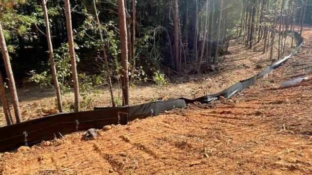 red land, freshly dug by tree line, with black barrier in front of trees