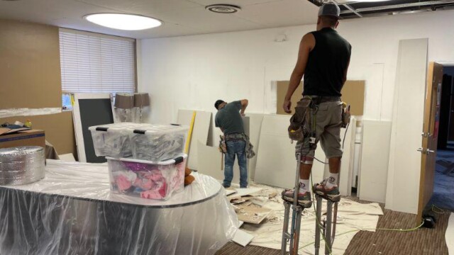 Worker on stilts waits for next ceiling tile being cut to size