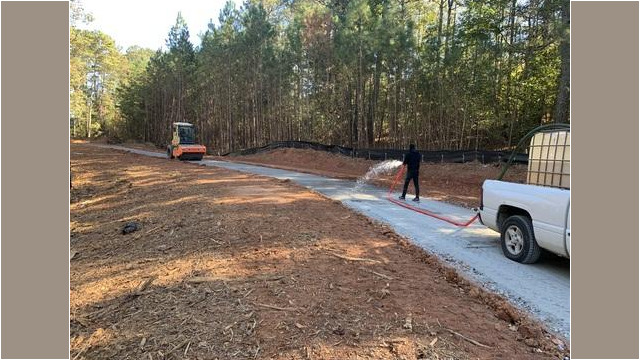 man spraying water on trail as steamroller follows