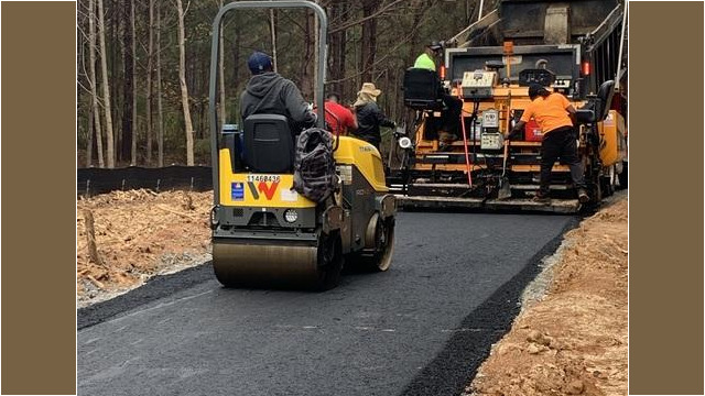 view of smoothing vehicle as men pour asphalt