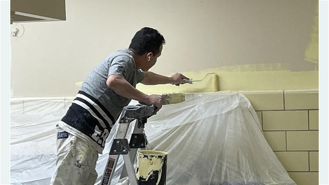 Worker on ladder painting the walls with a paint roller and brush