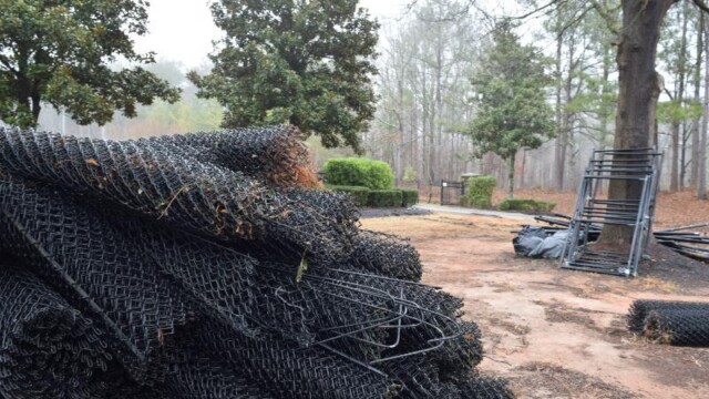 Chainlink fencing rolls piled up and gates leaning on a tree