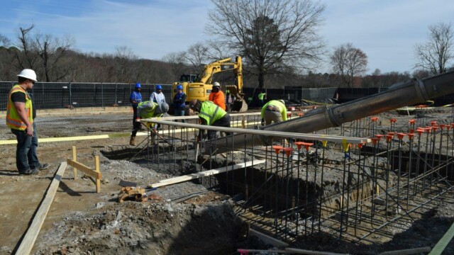 view from slide as concrete comes out of truck and workers guide it. Other workers look on.