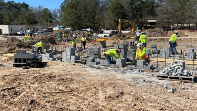 Seven construction workers in various stages working with cinder blocks